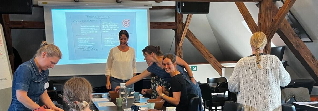 3️⃣ Billede: Smilende team, der taler åbent ved bord. Alt‑tekst: "Psykologisk tryghed og feedbackkultur som del af teamsamarbejde."